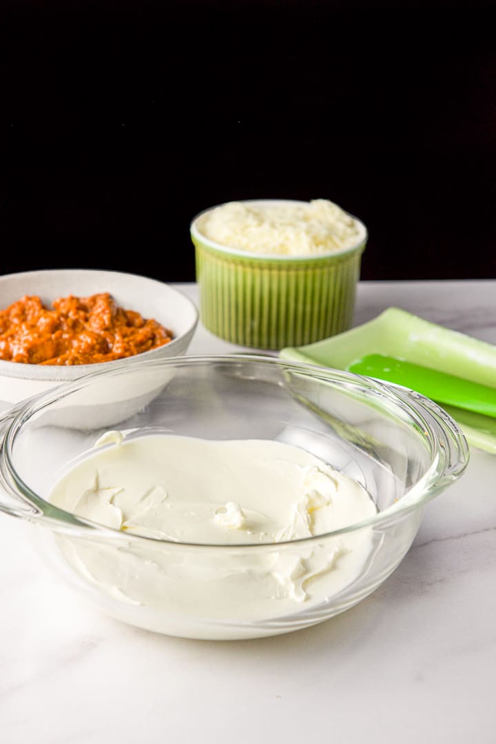 Cream cheese spread on the bottom of a baking dish with chili and mozzarella cheese in the background