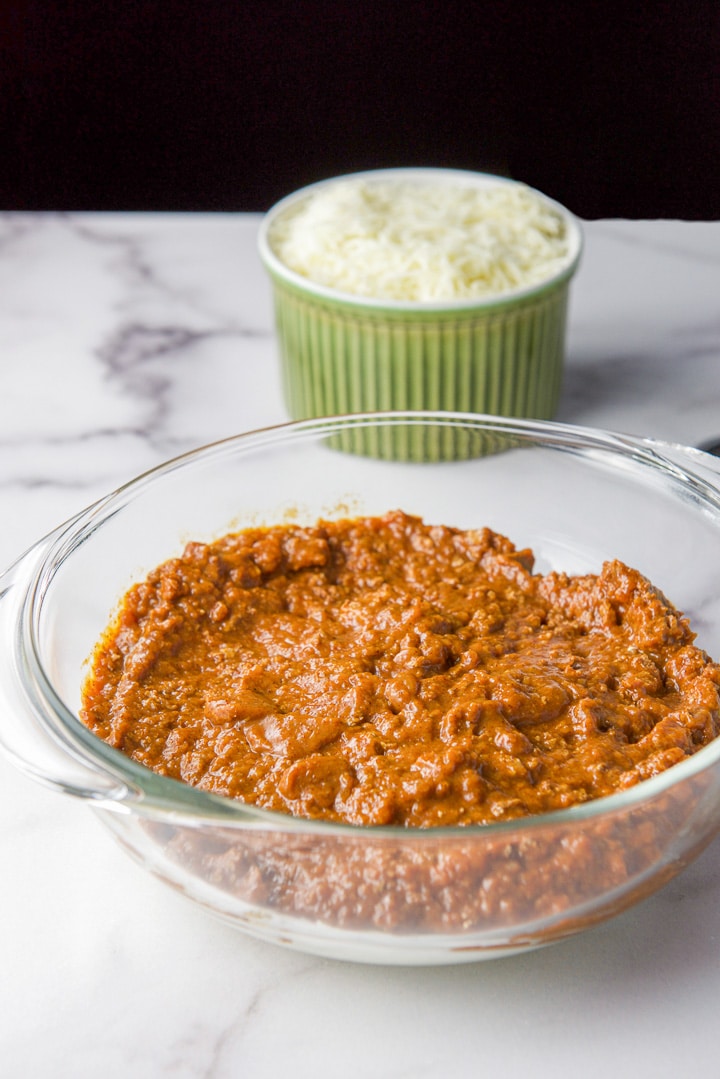Chili spread over the cream cheese with mozzarella cheese in the background