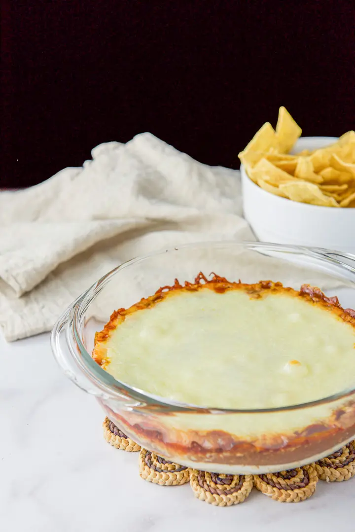 A clear bowl with a cheesy dip and a bowl of chips in the background