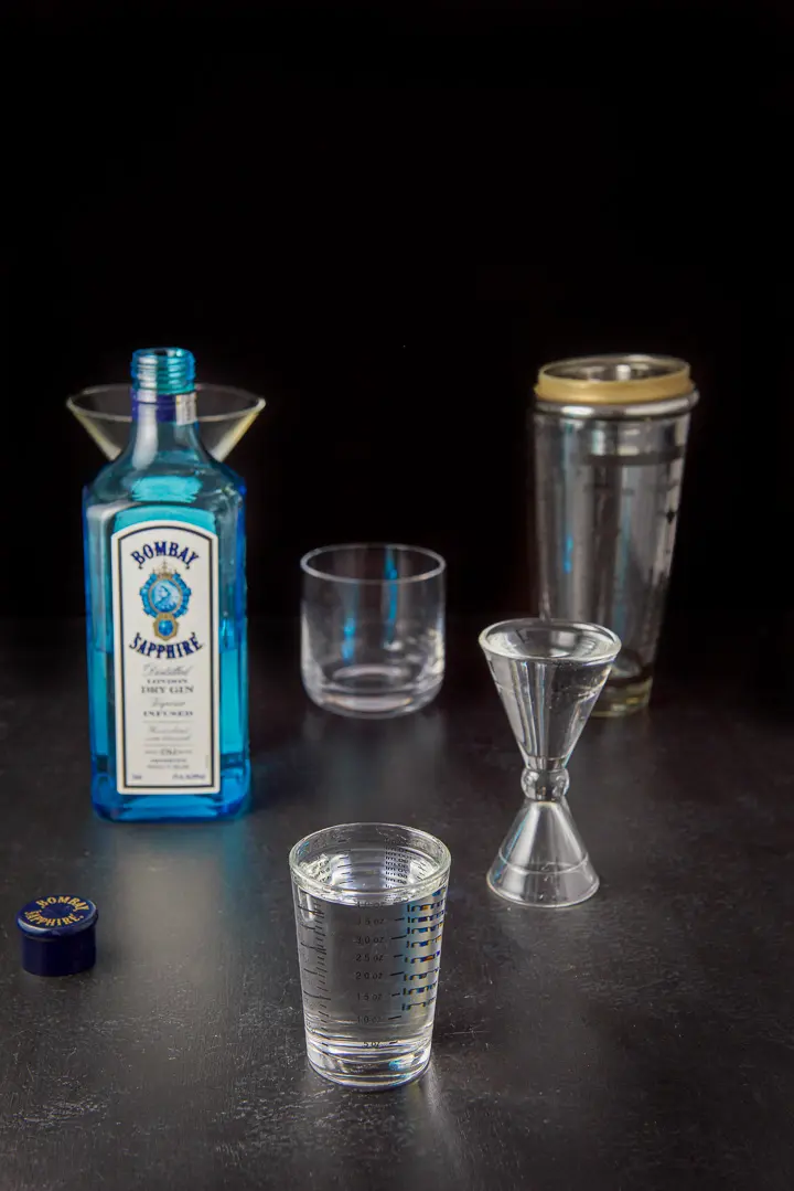 Gin measured with the bottle, shaker and glasses in the background