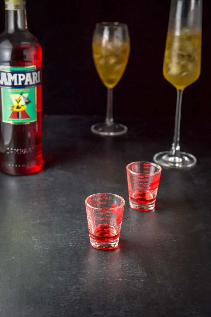 Campari poured out with the bottle and glasses in the background