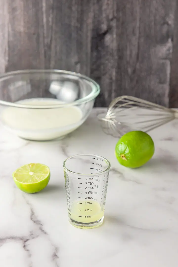 Lime juice measured out with a whisk, bowl of cream and limes