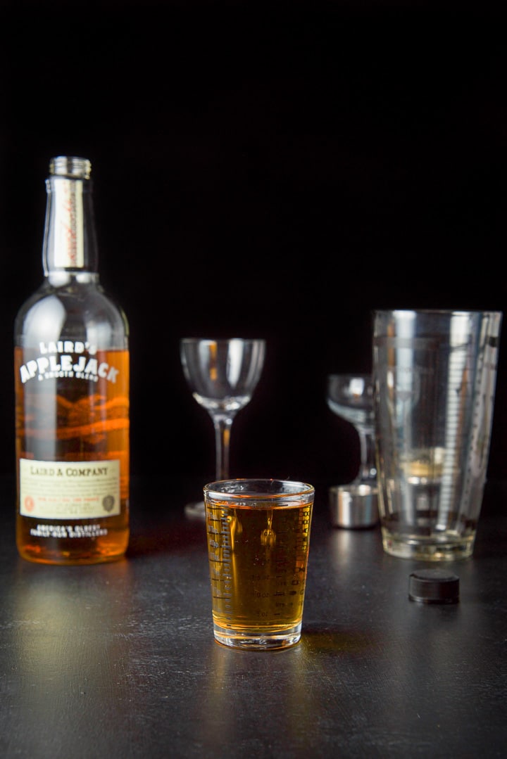 AppleJack liquor measured out with the bottle, shaker and glasses in the background