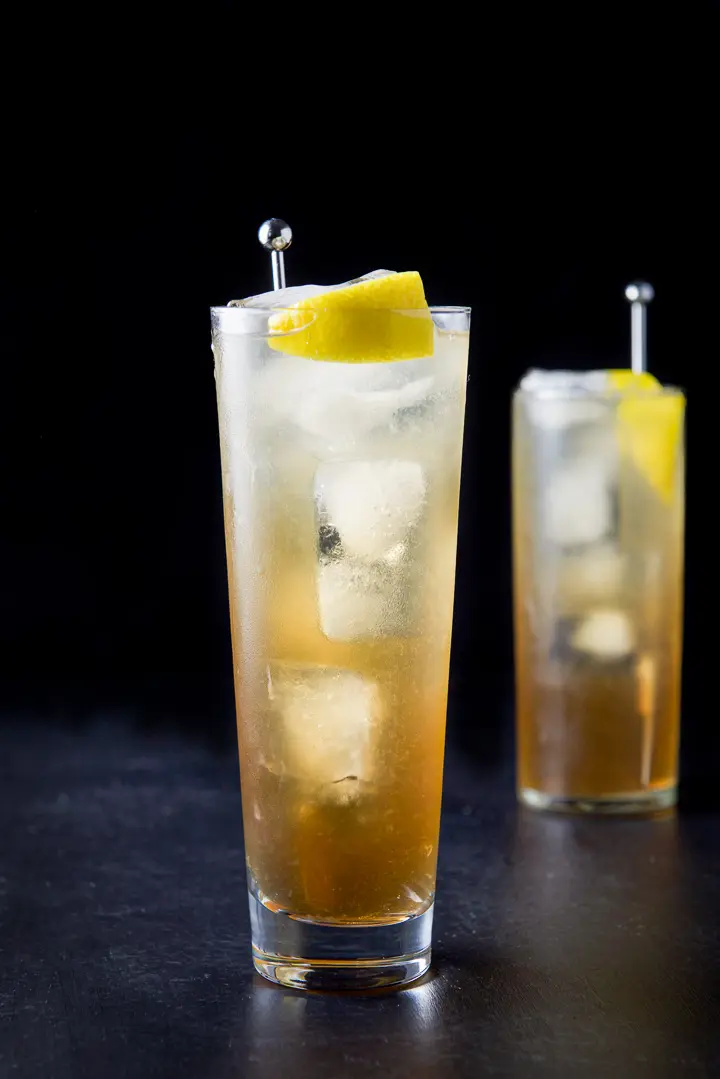 Vertical view of the wider glass filled with the potent cocktail with a lemon wedge and stirrer