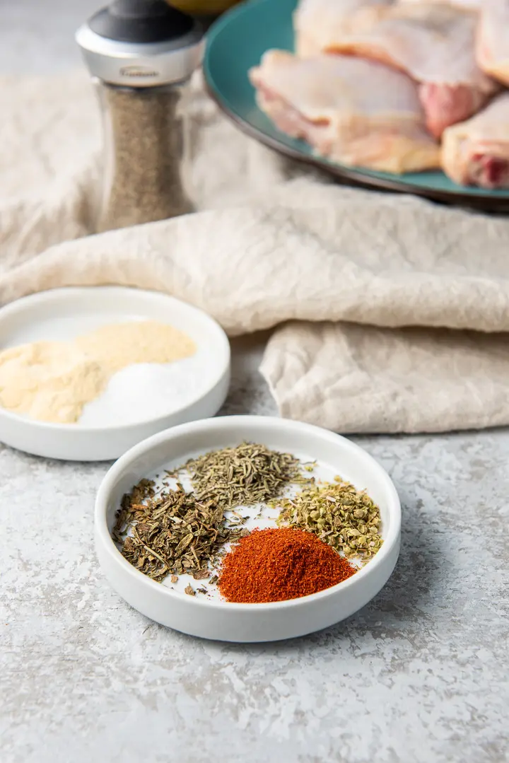 Oregano, thyme, tarragon, paprika, garlic powder, onion powder and chicken thighs on a table