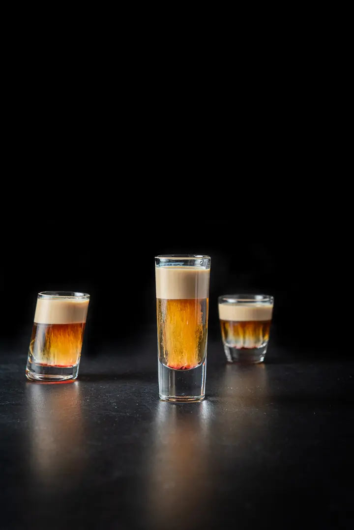 Vertical shot of the tall glass of the layered shot with the smaller glasses in the background