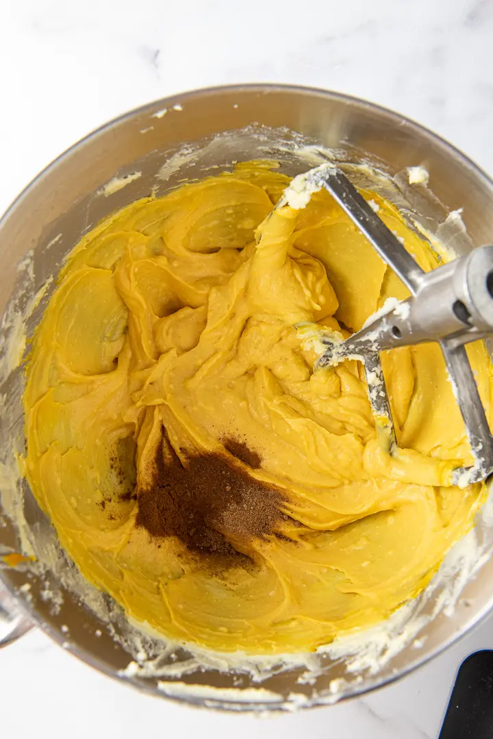Butter, sugar and pumpkin mixed with the spices on top in a metal mixing bowl