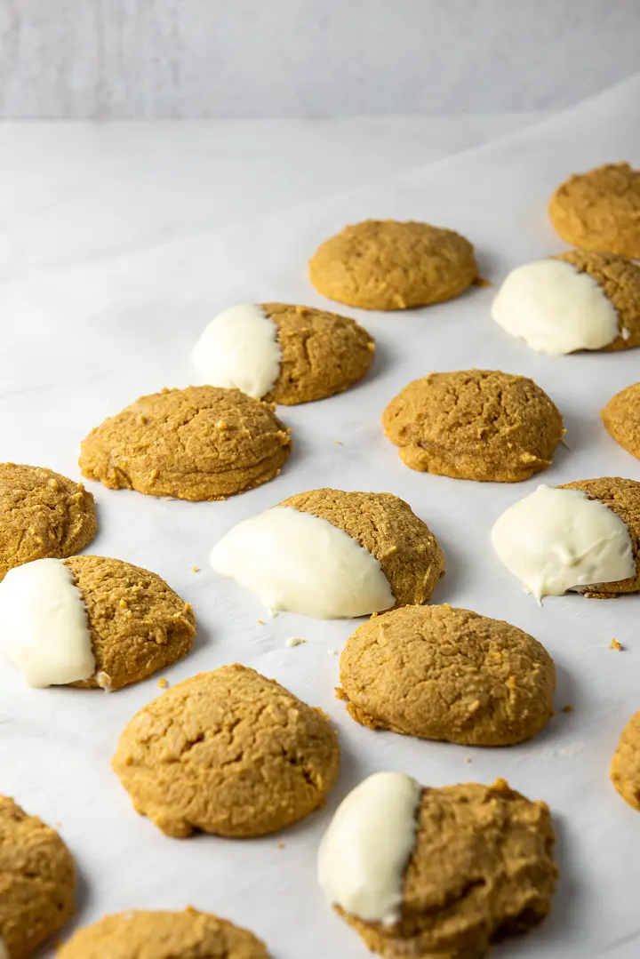 Parchment paper filled with pumpkin cookies, some dipped in white chocolate