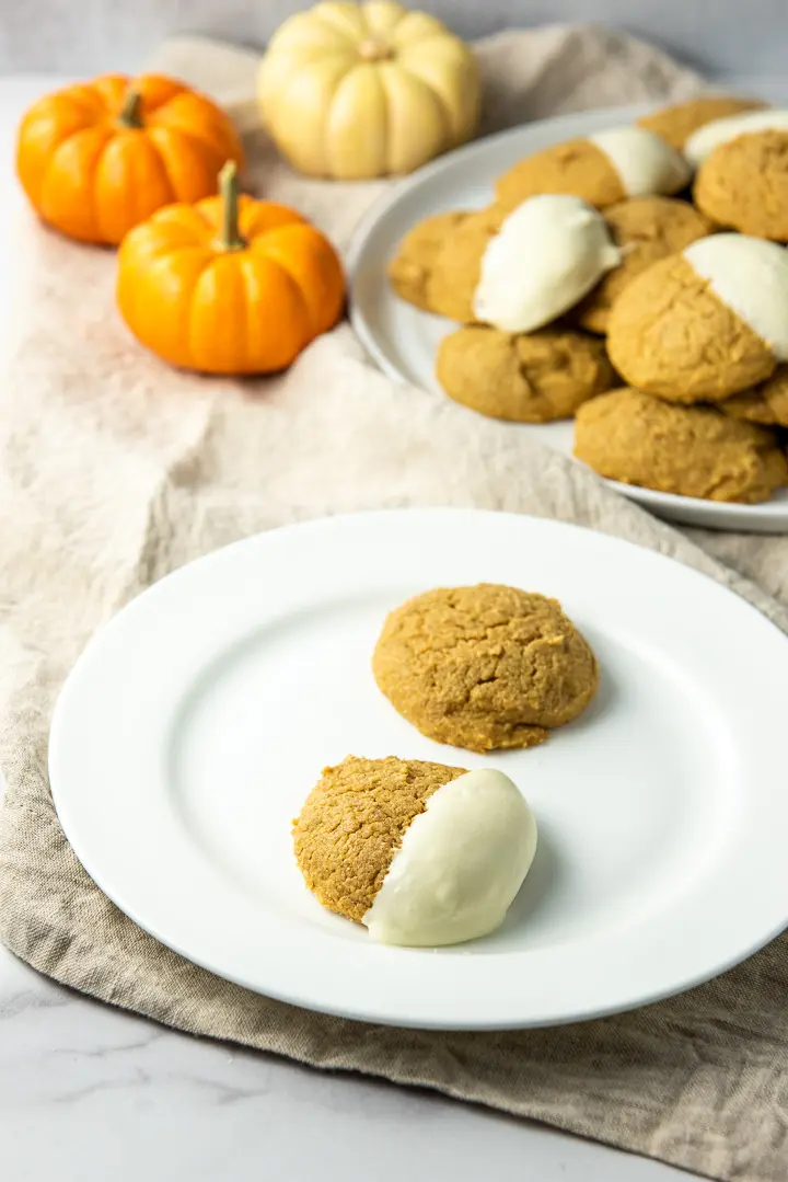 Close up of a plate of two pumpkin cookies, one plain and one dipped in white chocolate