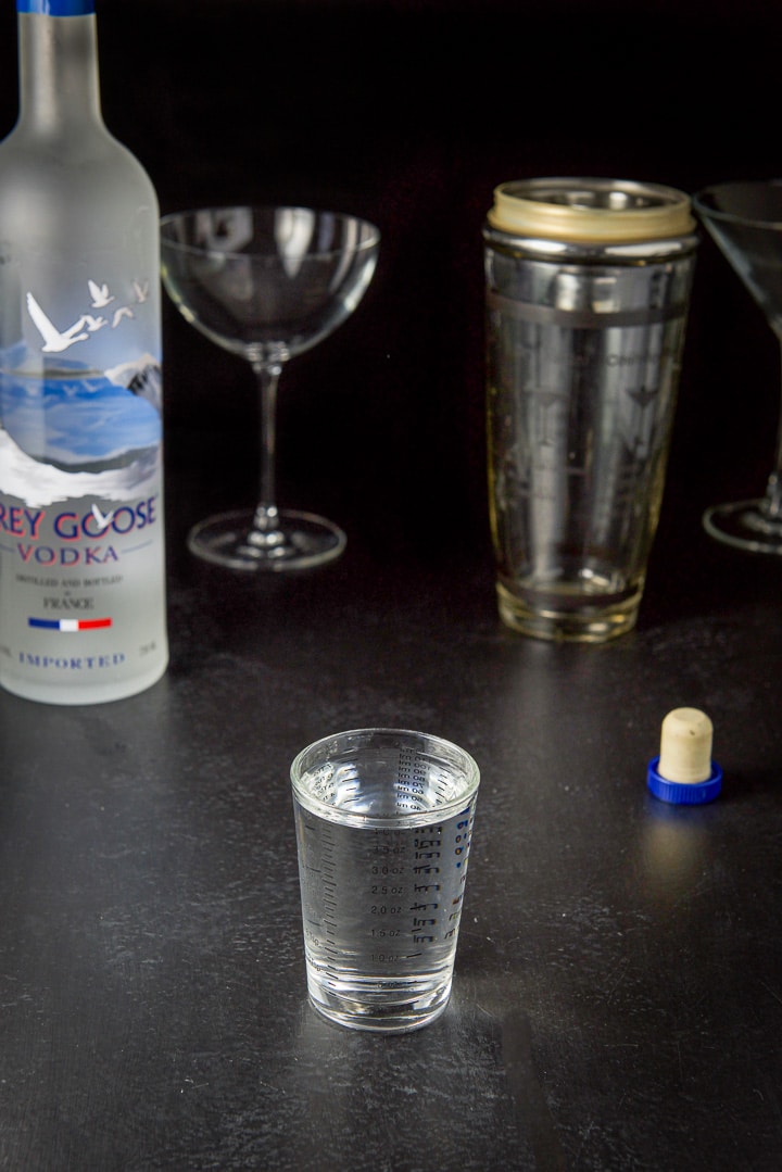 Vodka poured out with the bottle, shaker and glasses in the background