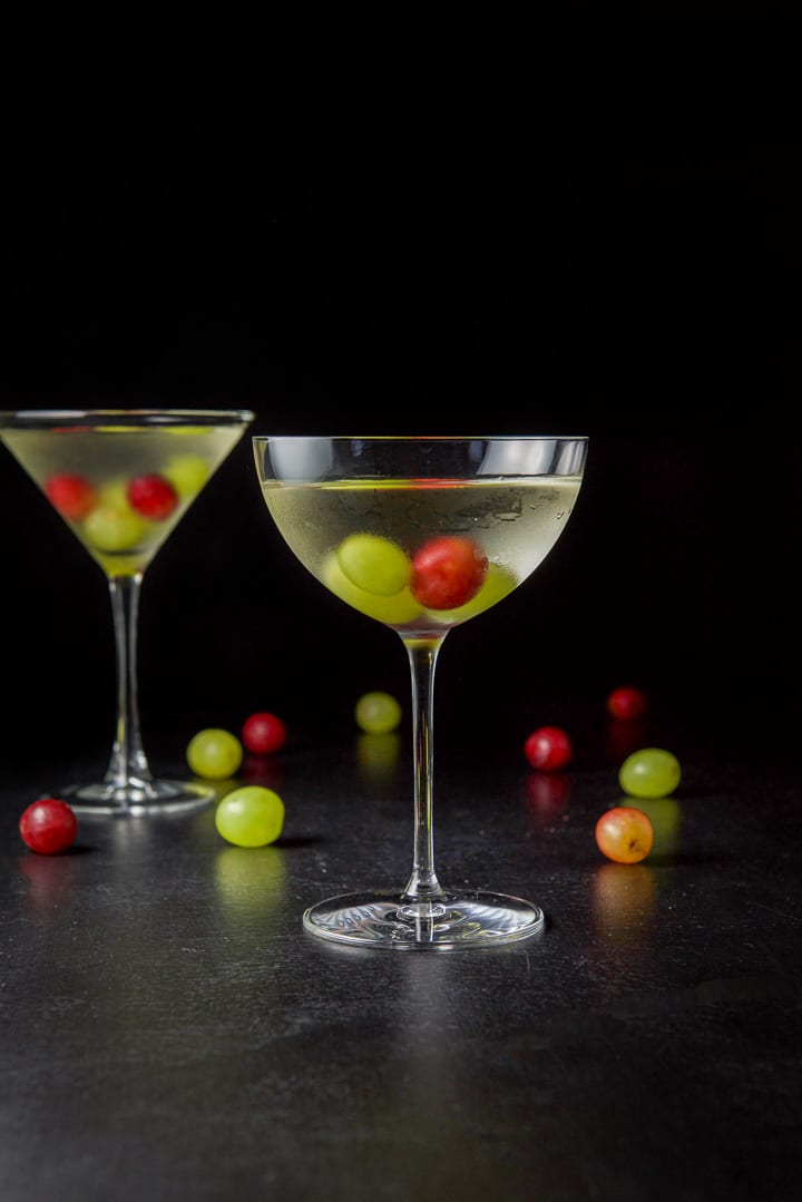 Vertical view of the wide glass filled with the cosmo with grapes in the glass and on the table