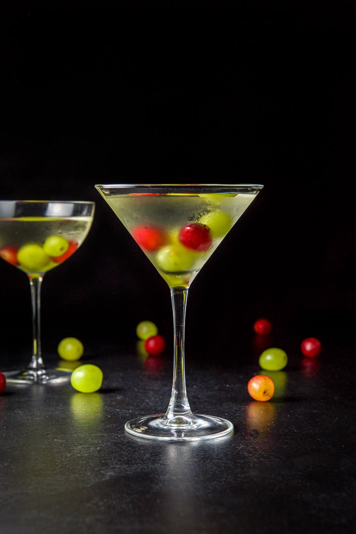Vertical view of the classic martini glass filled with the grape cosmo with grapes in it and strewn on the table