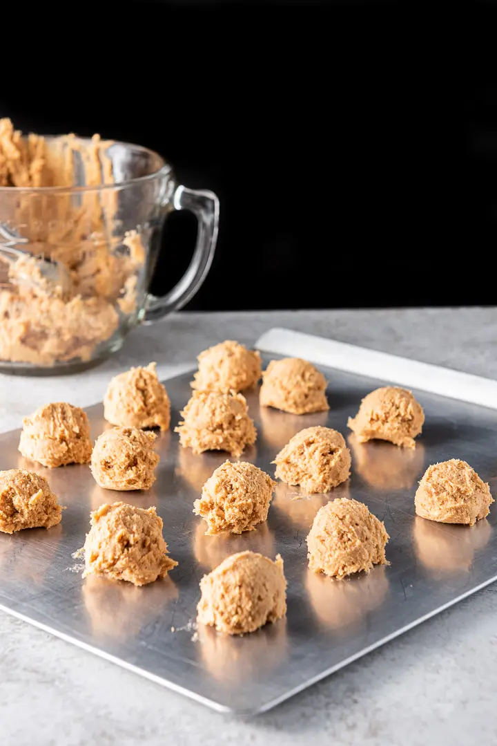 Balls of butterscotch cookies batter on a cookie sheet with the glass bowl in the background