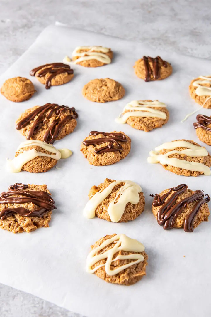 A large piece of parchment paper with butterscotch cookies on it and chocolate drizzle on them
