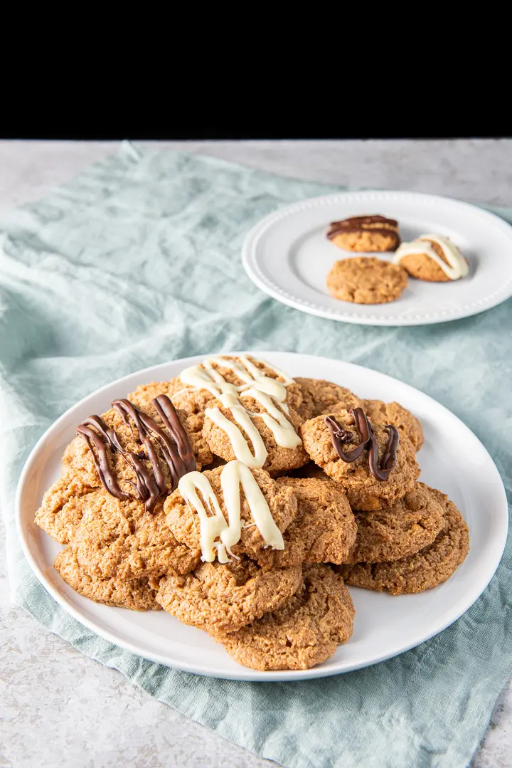 A pile of cookies on a big white plate with a few cookies on another plate behind it