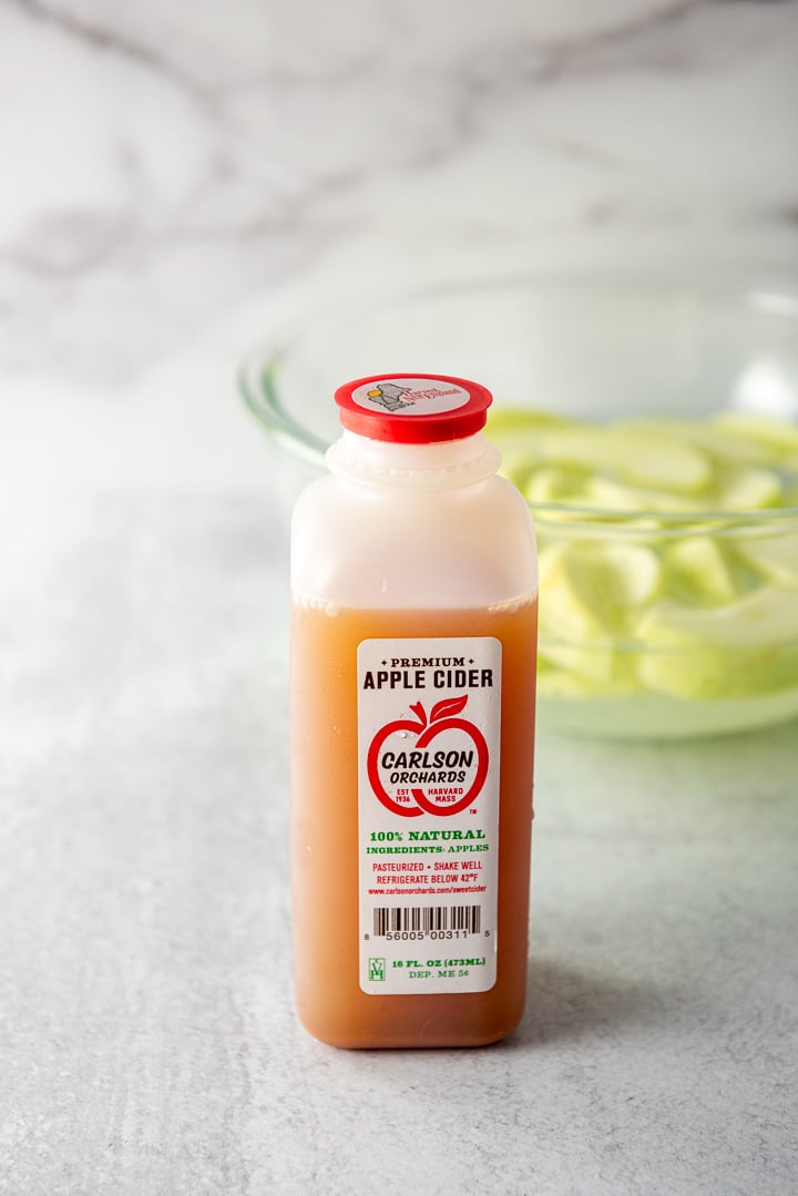 Apple cider in front and a glass bowl with apples soaking in lemon and water