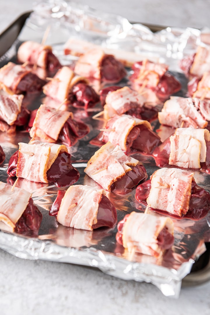 A jellyroll pan with a bunch of chicken livers rolled up in bacon