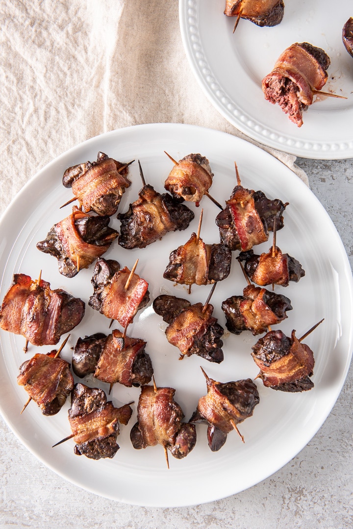 Aon overhead view of a big white plate with livers wrapped in bacon on it and a smaller white dish in the upper right
