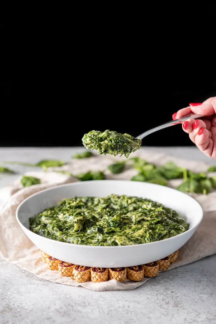A spoonful of spinach held over a white bowl of it