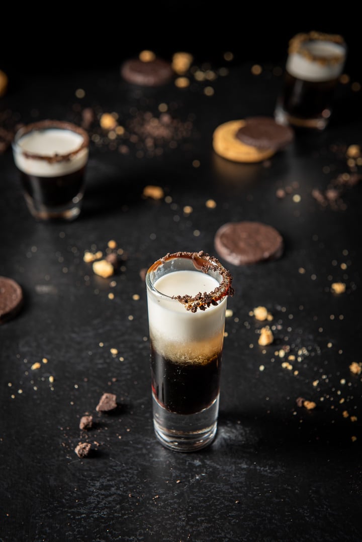 Close up for the three shot glasses filled with the cookie shot. The tall glass in front. There are cookies also on the table