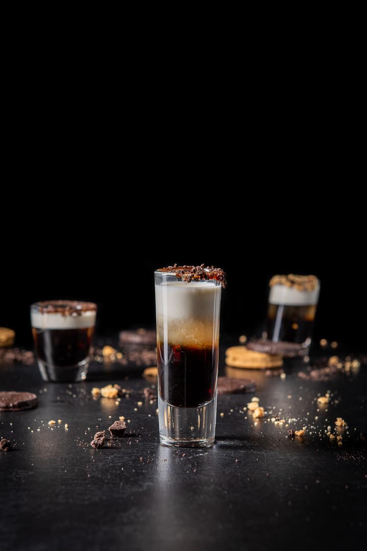 Vertical view of the cookie shot. The tall glass is in front and two other glasses are in the background along with cookies crumbs