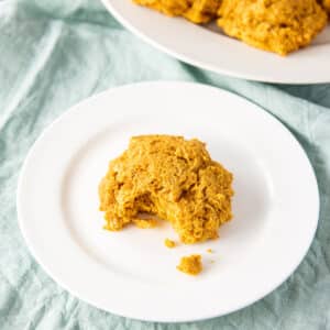 Square photo of a potato biscuit on a white plate with more in the background - square