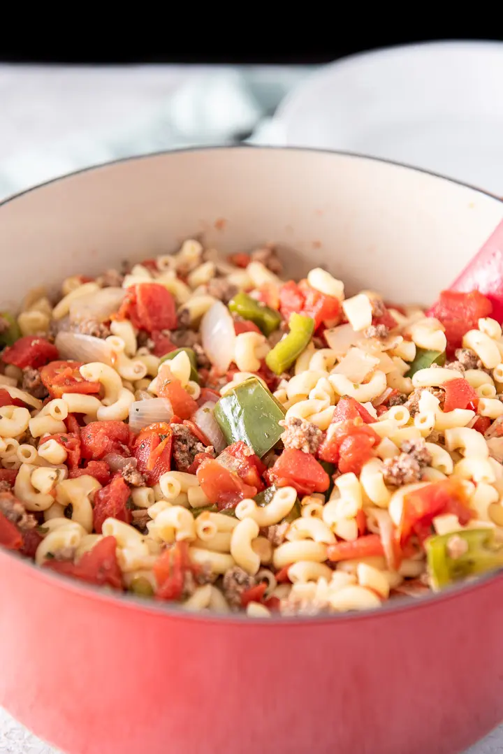 A big red pan full of elbow macaroni, ground beef, tomatoes, peppers and onions