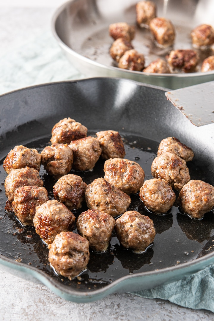 Saut&eacute;ed meatballs in a cast iron pan with other meatballs in the background