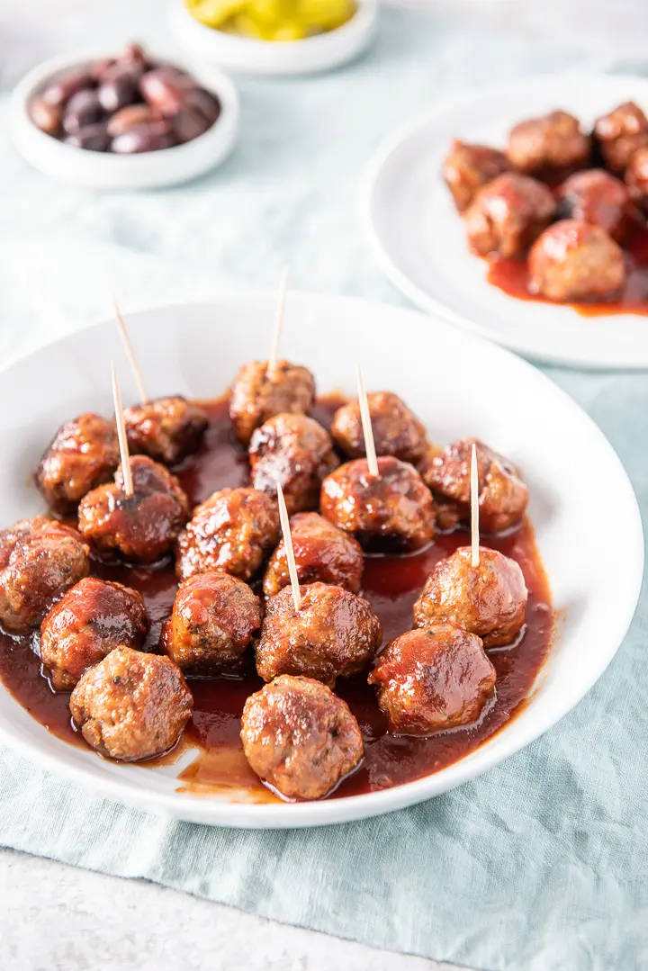 A white shallow bowl with the meatballs in bourbon sauce with others in the background