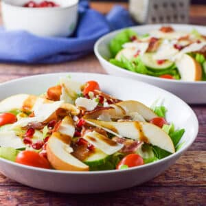 Colorful salad in two shallow bowls with pomegranate seeds in the background - square