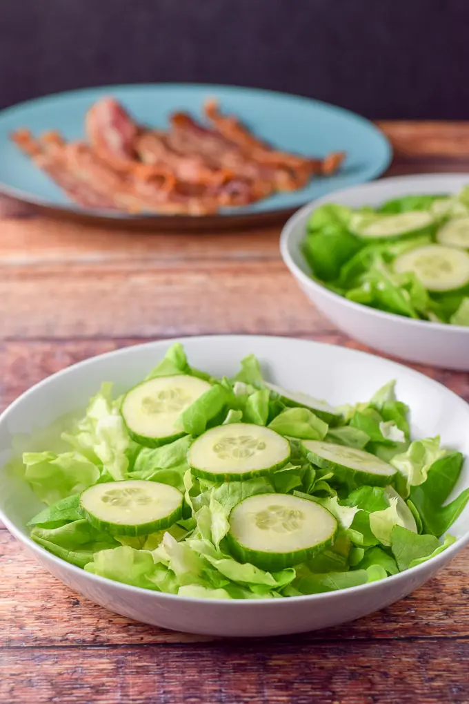 Boston lettuce and cucumber slices with the bacon on the plate in the background