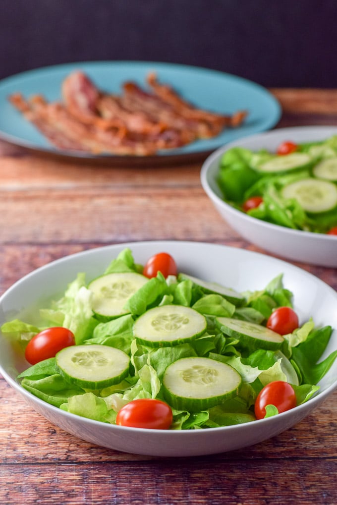 Cherry tomatoes added to the salad with bacon in the background