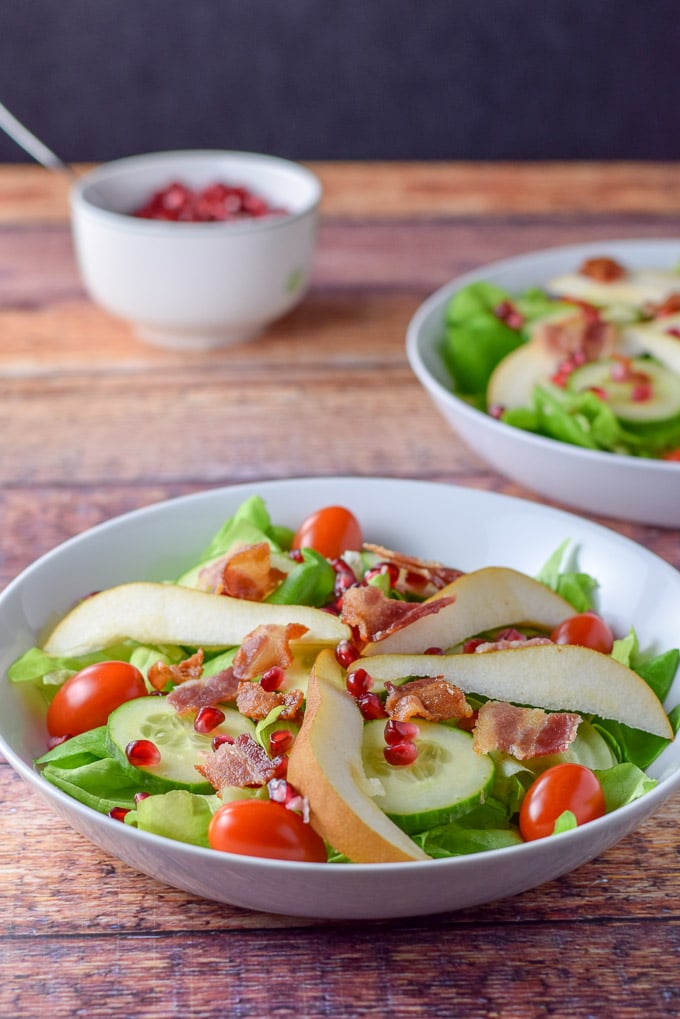 Bacon crumbled on the salad with a bowl of pomegranate seeds in the background