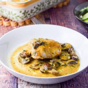 A shallow white bowl filled with a chicken thigh with sauce and mushrooms in it
