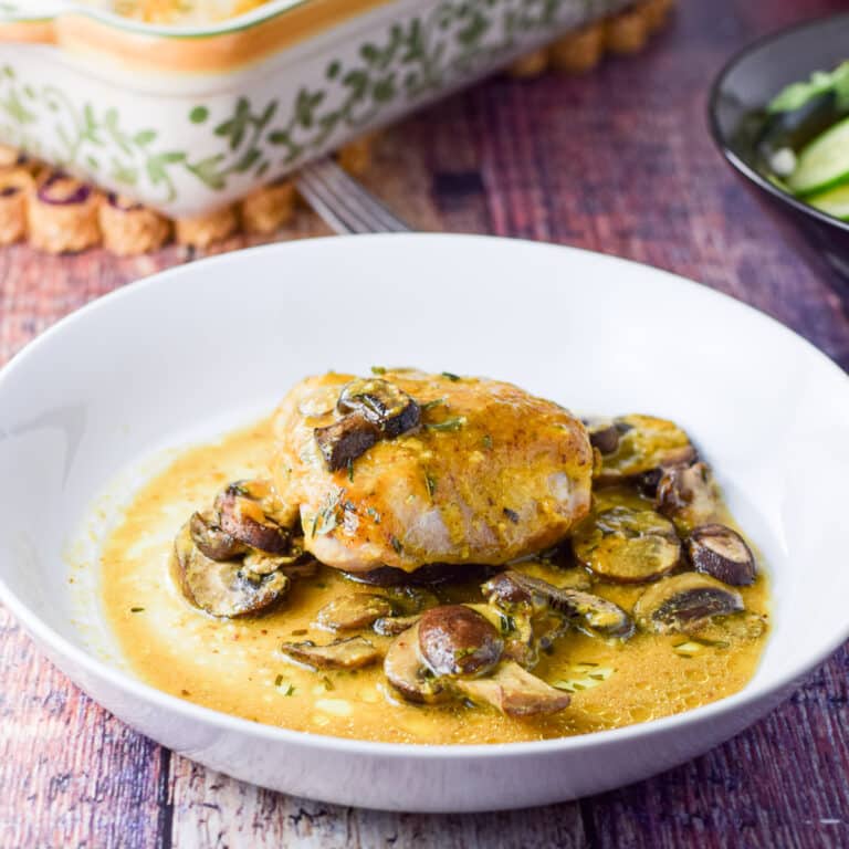 A shallow white bowl filled with a chicken thigh with sauce and mushrooms in it