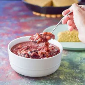 Spoonful of fig sauce held over a white bowl with cornbread in the background - Square