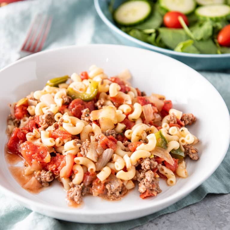 white shallow bowl of pasta chop suey with a salad in the background