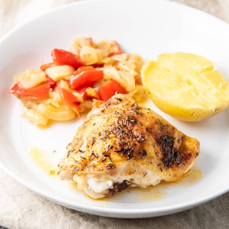 Square photo of the chicken thighs on a plate with vegetables and a potato