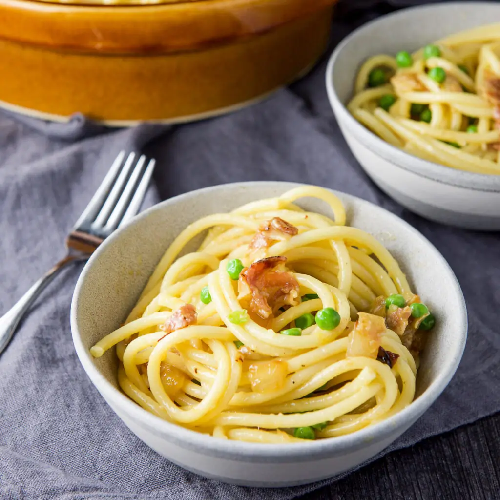 Pasta carbonara in a grey bowl with a fork and another bowl in the background - square