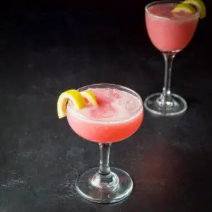 Coupe glass filled with the pink cocktail with a lemon twist in it - square