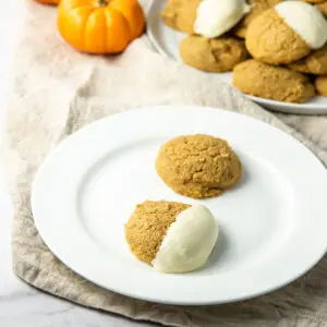 Pumpkin cookies on a plate, on dipped in white chocolate and the other plain - square