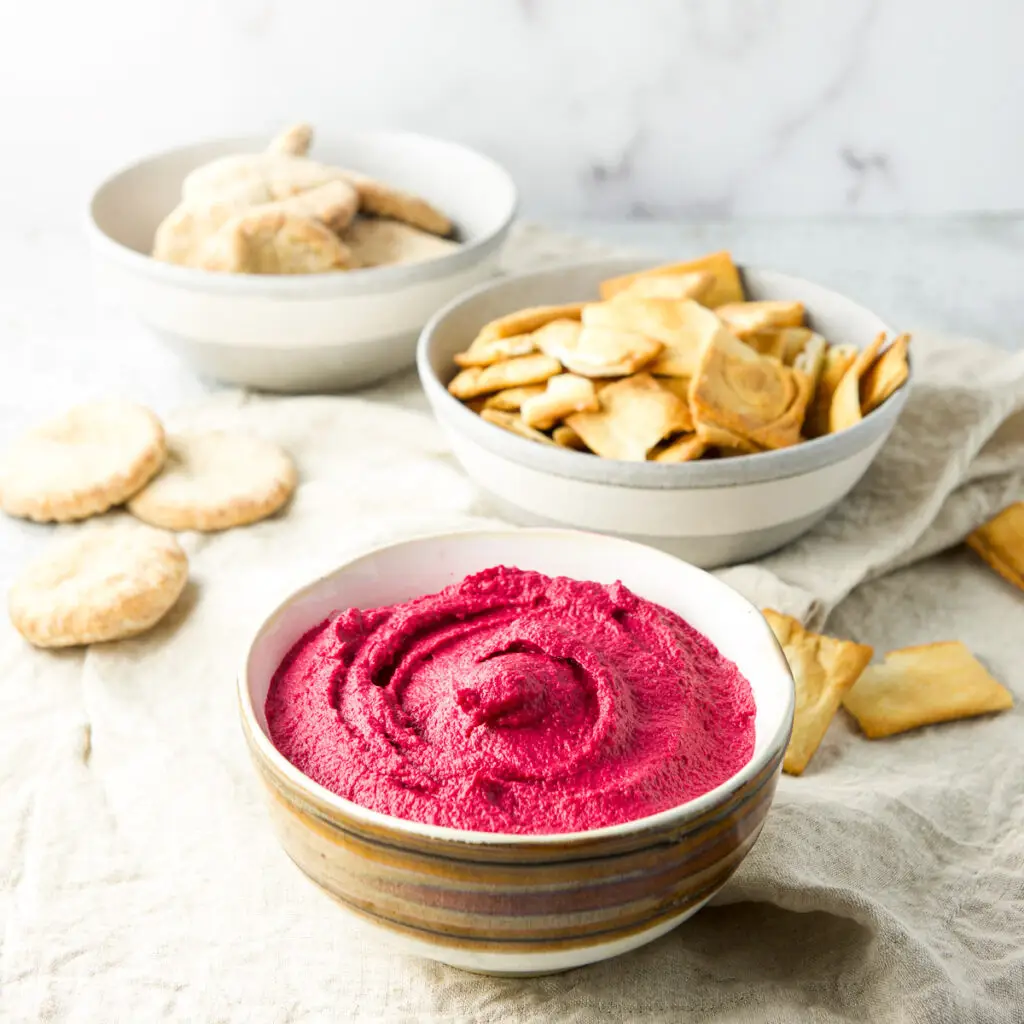 Close up of a bowl of beet hummus with pita in the background
