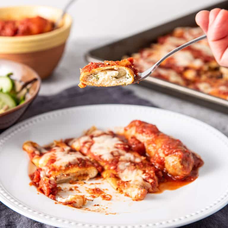 A forkful of manicotti over a plate