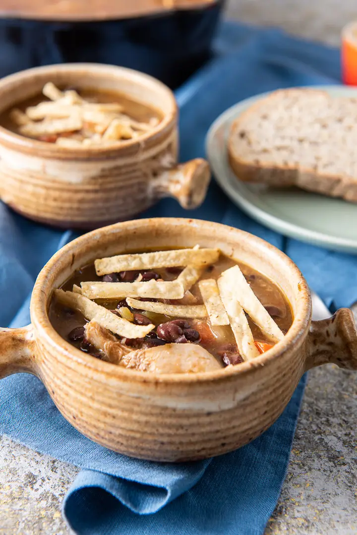 close up of the soup in crocks with tortilla strips on top and bread in the background
