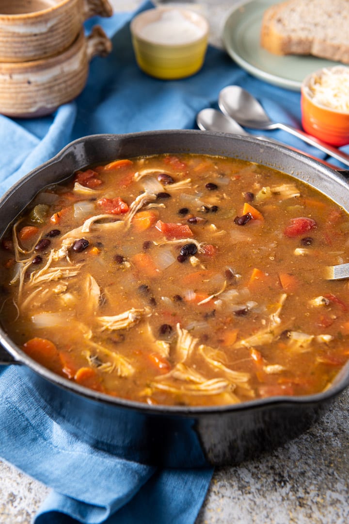 Pan of chicken tortilla soup with bread in the background