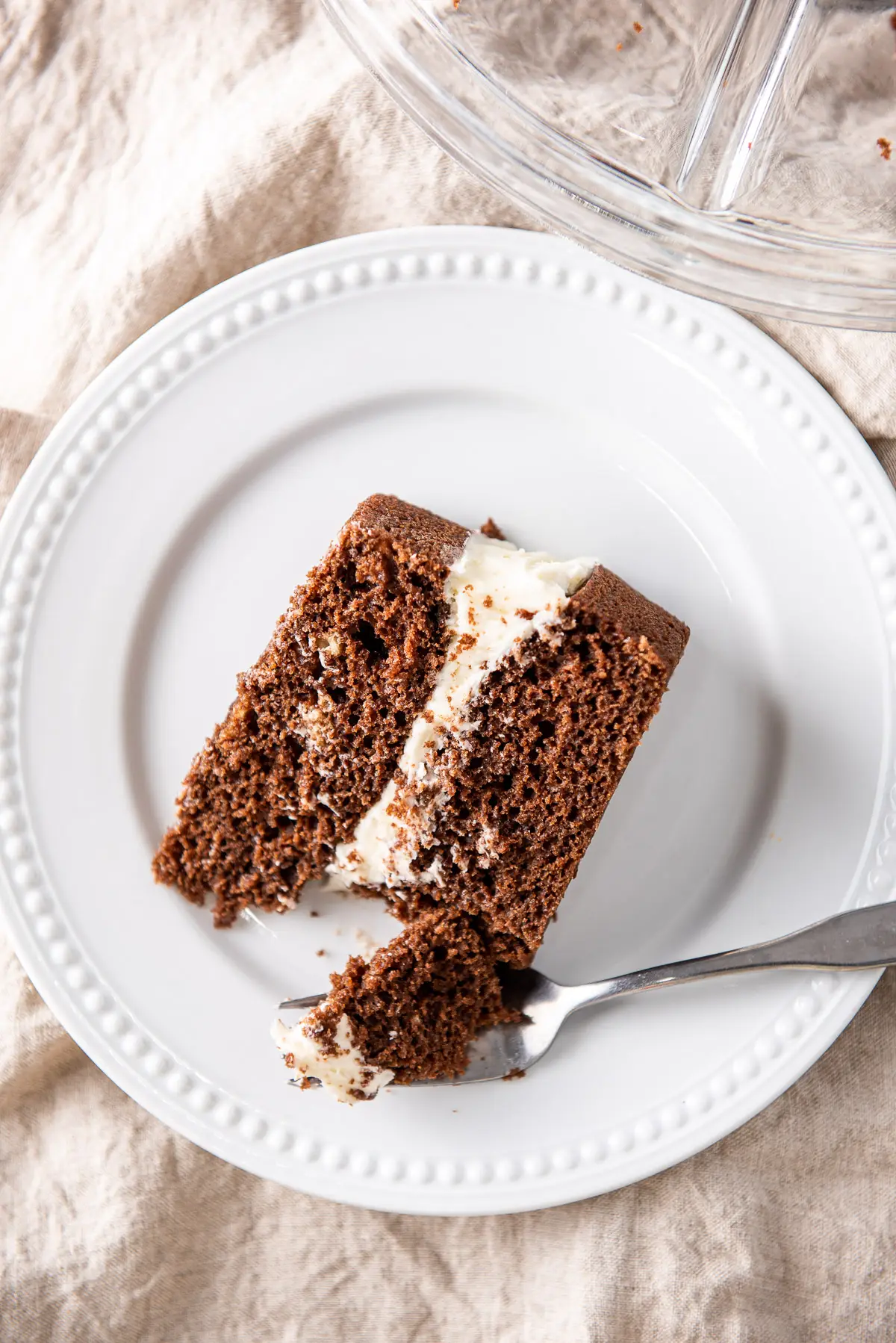 Overhead view of a white plate with a layered chocolate cake. There is a fork with a piece of cake on it