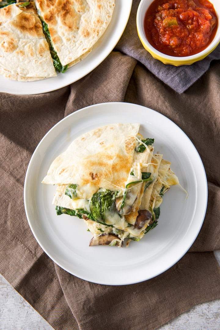 Spinach and mushroom quesadillas stacked on a plate with salsa