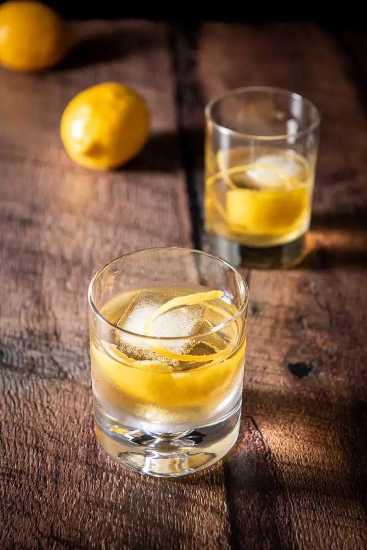 Two double old fashioned glasses filled with the rusty nail with lemon twists