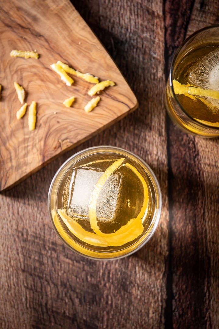 Overhead view of the cocktail with lemon twists and a cutting board with some lemon rind shavings