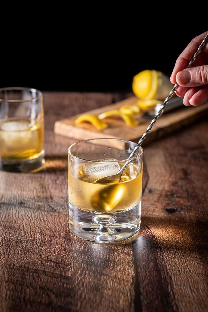 A female hand stirring the cocktail with a cocktail spoon